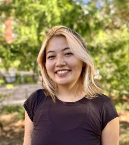 Headshot in black short-sleeve t-shirt in front of green foliage