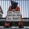 Protester in detainee garb holding sign, "I am still waiting for your humanity"