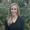 Headshot of Elizabeth in a longsleeved black v-neck short in front of greenery